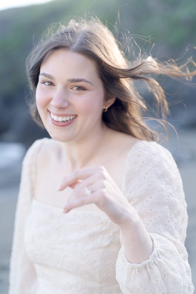 Newly engaged girl shows her engagement ring and smiles at the camera.