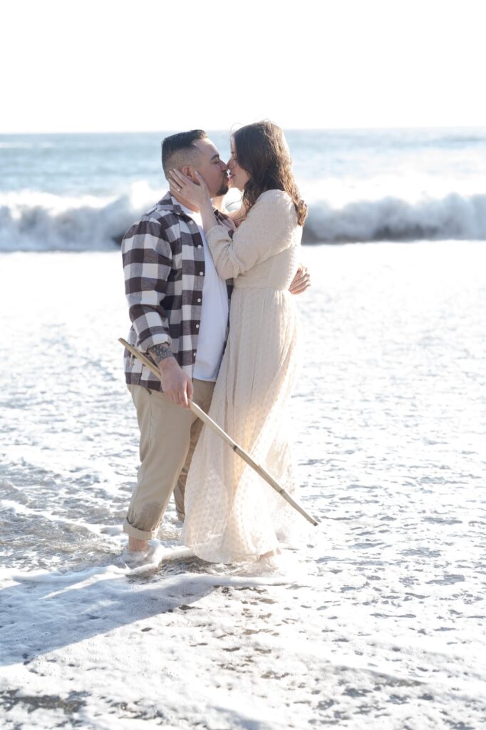 Newly engaged couple kiss in shallow waters at Bodega Bay beach.