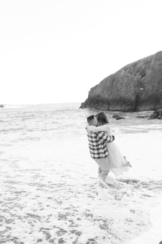 Man lifts his fiancee at the beach for a kiss.