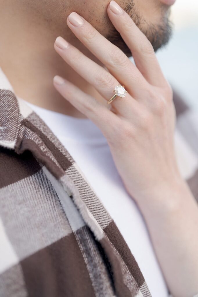 Lady puts her hand with an engagement ring on her lover's cheeks.