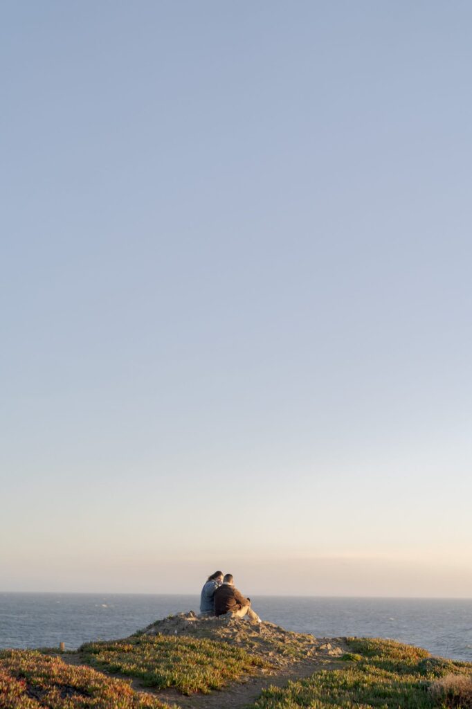 Young man and girl sit together at a hillside and look at the ocean view in Bodega Bay.