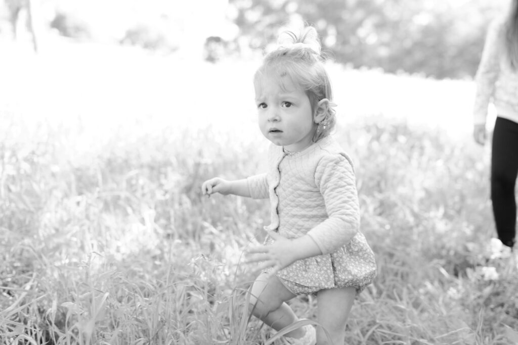 Adorable baby girl walking in an open, overgrown field.