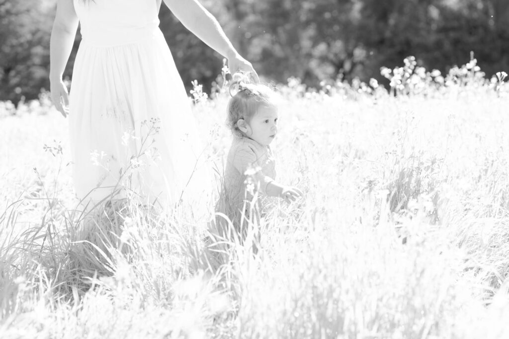 Baby daughter leads her mom into the grassy fields.