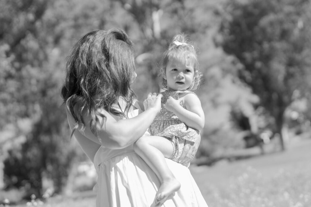 Mom adjusts her baby daughter's clothes while the little one looks away.