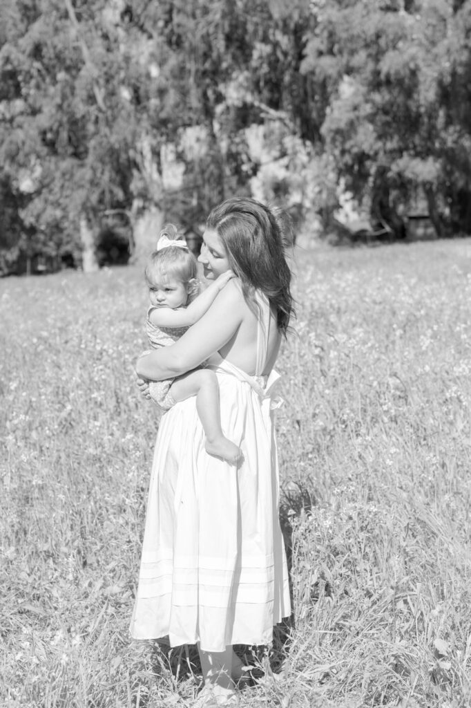 Tall grasses, wild flowers, lady in wite gown holding her baby daughter.