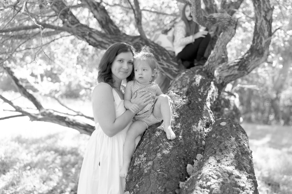 Jilian smiles at the camera while placing her baby daughter on a tree trunk.