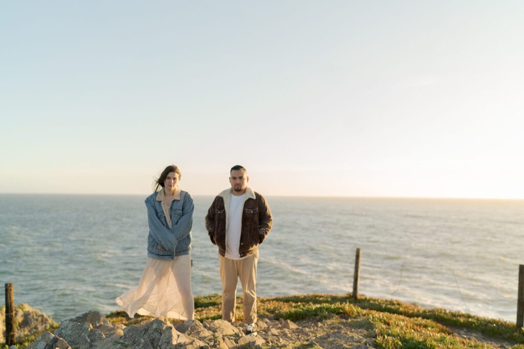 Man and lady stand atop a hill by Bodega Bay duriign sunset.