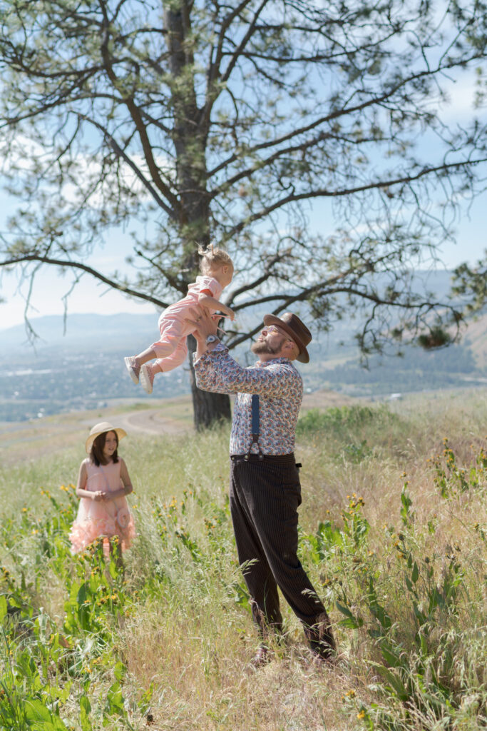 Dad hoists his baby in the air while his daughter watches into the La Grande landscape.