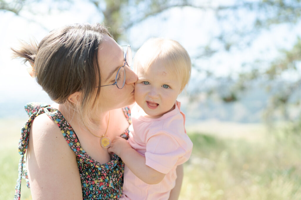 Lady wearing glasses kisses her baby who looks into the camera.