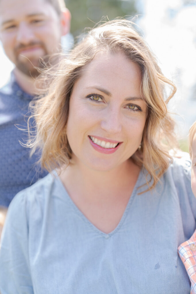 Mom looks lovingly at the camera while her husband smiles from behind.