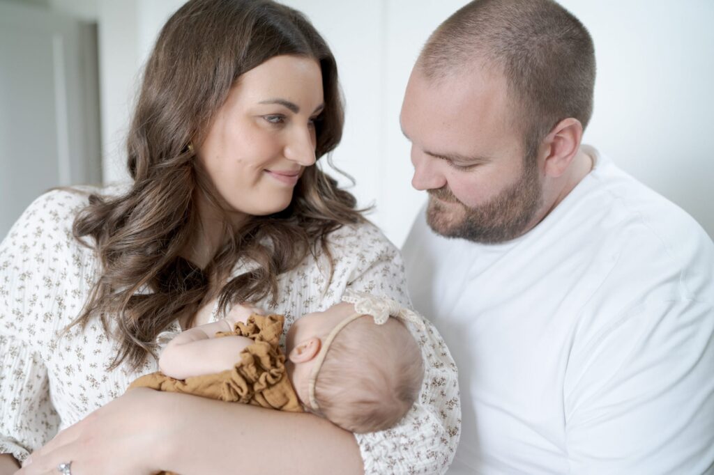 Mom holds her newborn and looks at her husband while he looks at the baby.