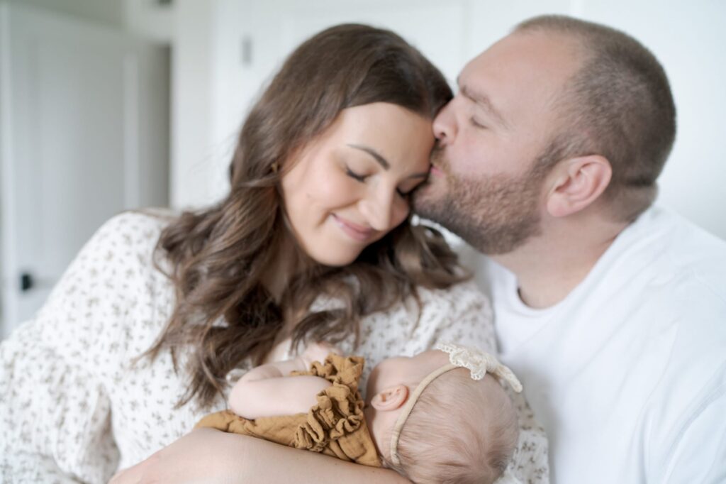 Father of a newborn baby kisses his wife.