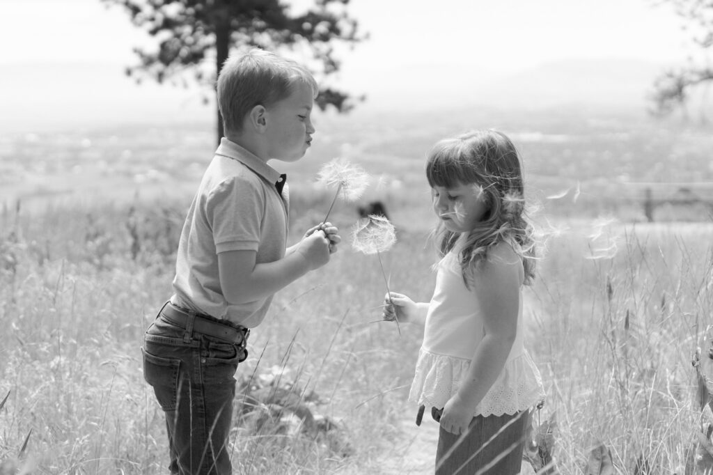 Professional Family Photographer Robin Jolin captures a Little boy and her sister blow dandelions in the La Grande outdoors.