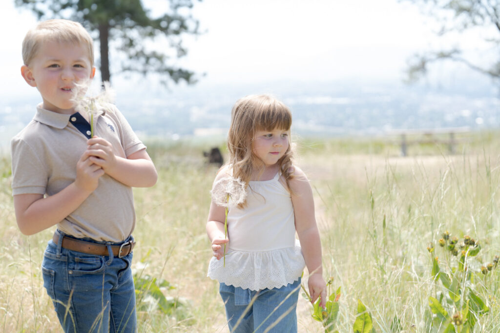 Baby girl and her brother hold dandelions.