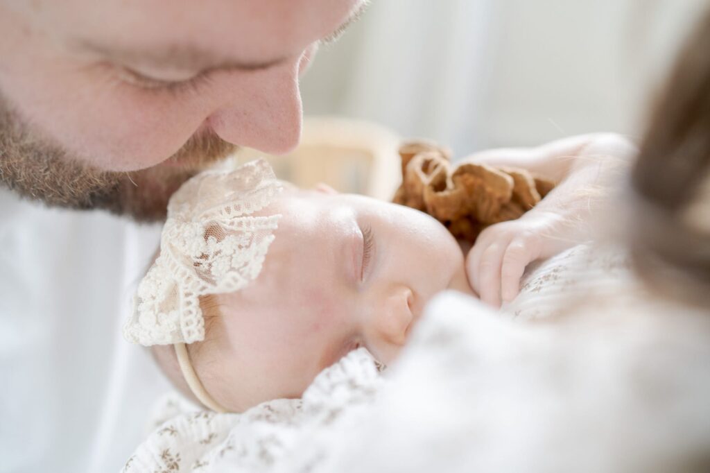 Father leans down to kiss his newborn baby wearing a cute hairband.