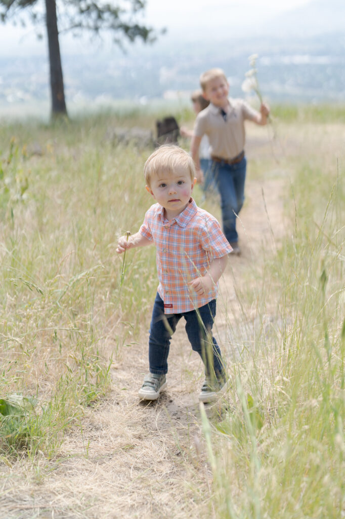 Baby boy in trousers and an orange checkered shirt walks in front of his elder brother.