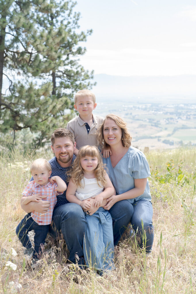 Family photography where the parents sit at the center, the father on the left with short brown hair and a beard, wearing a blue shirt and jeans, and the mother on the right with shoulder-length blonde hair, dressed in a light blue blouse and jeans.