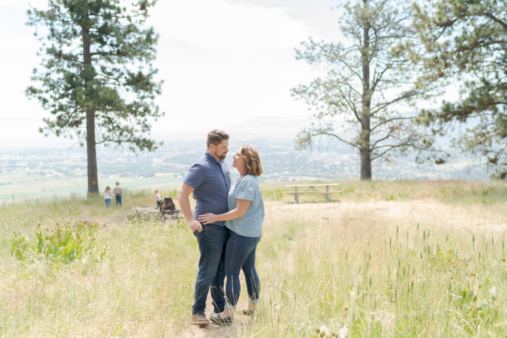 Mother and father embrace each other while their children play in the distant background.