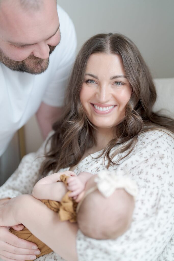 Dad looks at his newborn baby while his wife smiles at the camera.