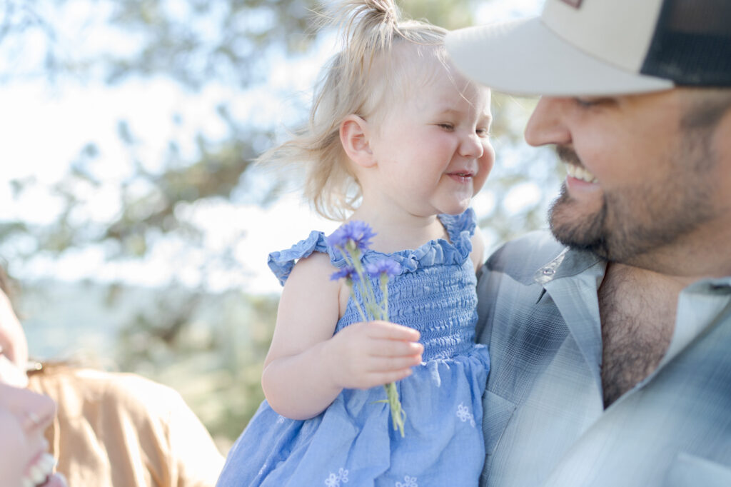 Little baby daughter smiles at her dad who holds her in his arms.