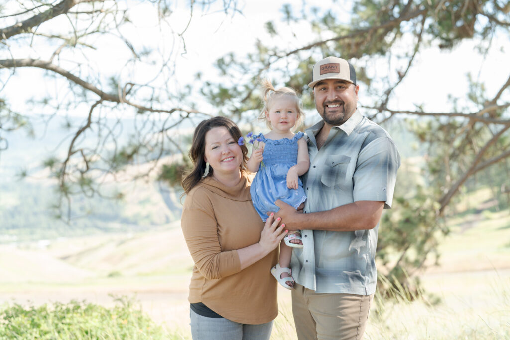 Mother and father hold her baby daughter at a hillside.