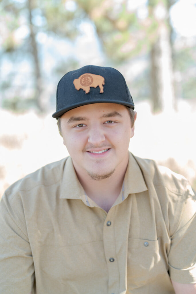 Young man in a light brown shirt and a black cap with a goatee.