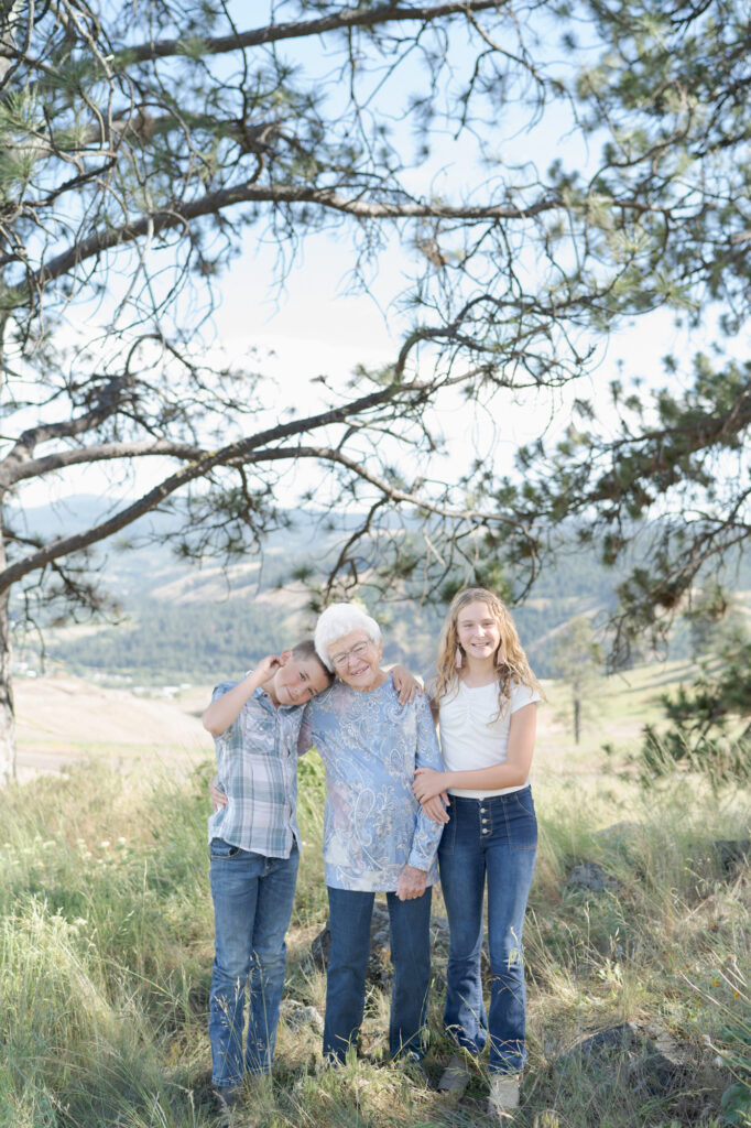 Grandma with gray hair holds her grandson and granddaughter.