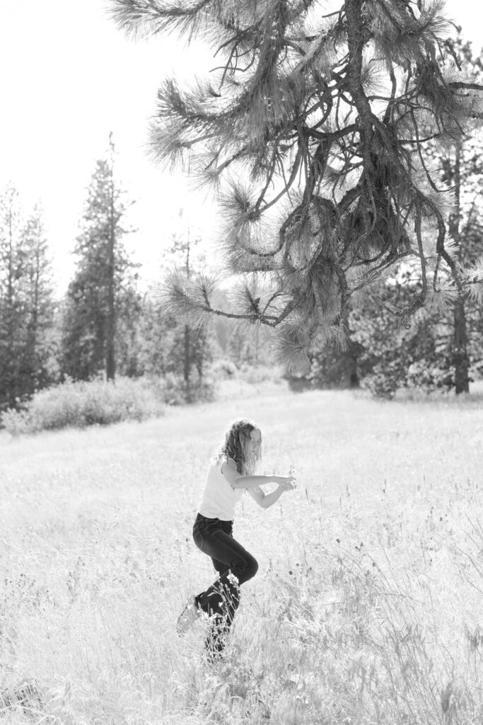 Teenage girl plays with wildflowers in a field with tall grass.