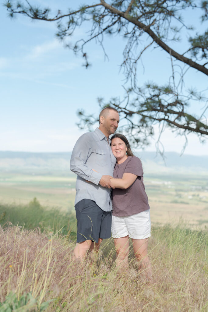 Mom and Dad embrace each other in a grassy field surrounded by trees