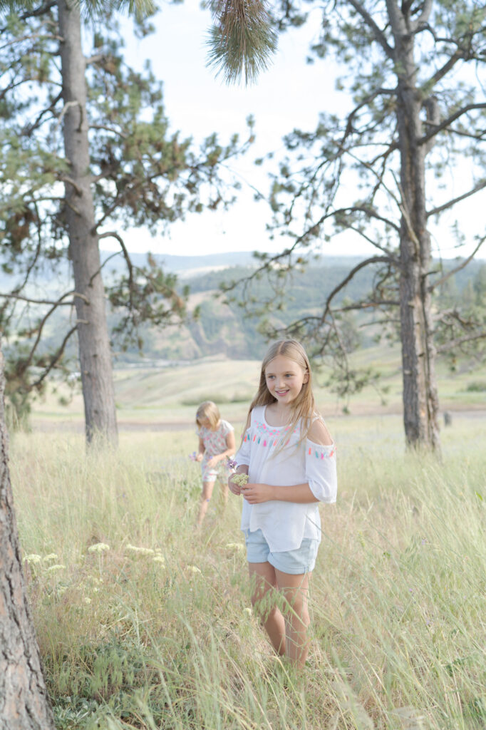 Two young girls collect wildflowers in a natural outdoor setting