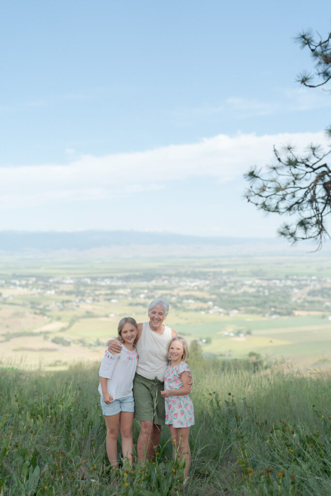 Granddaughters with their grandmother in front of a far-spread landscape.