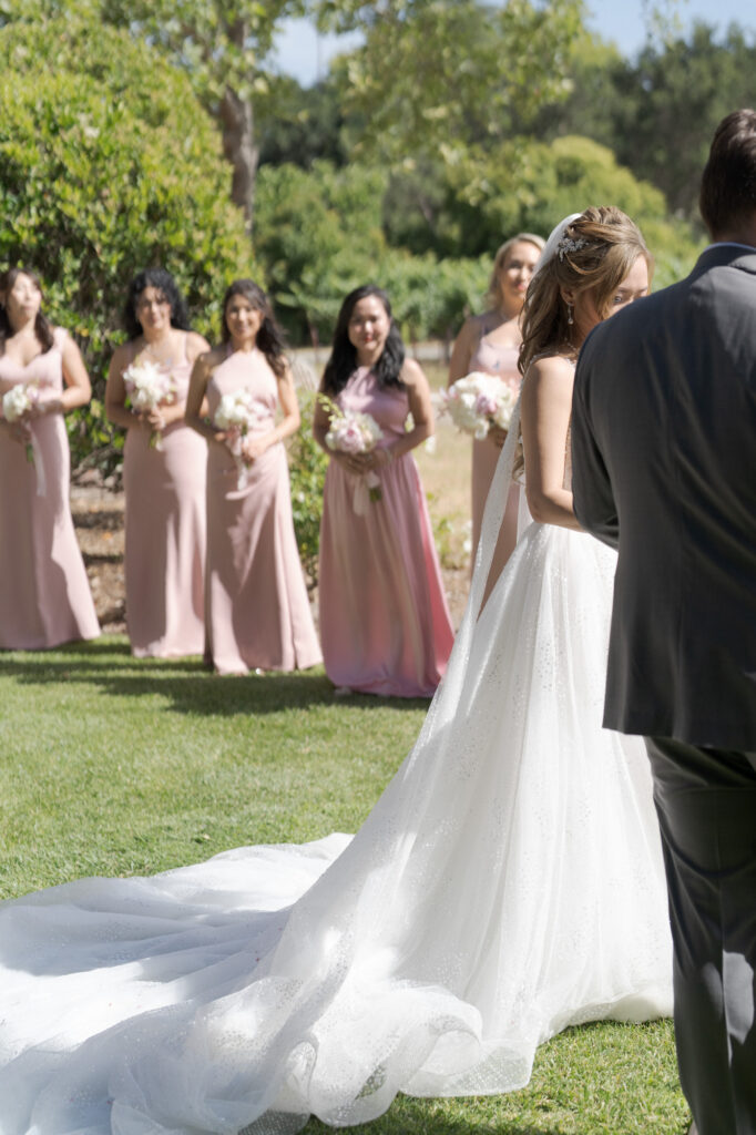 Bride and groom at the wedding ceremony with bridesmaids holding bouquets of flowers in the background.