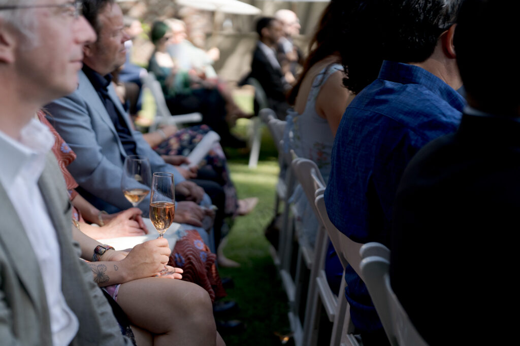 Guests seated in rows hold glasses of champagne at a wedding ceremony.