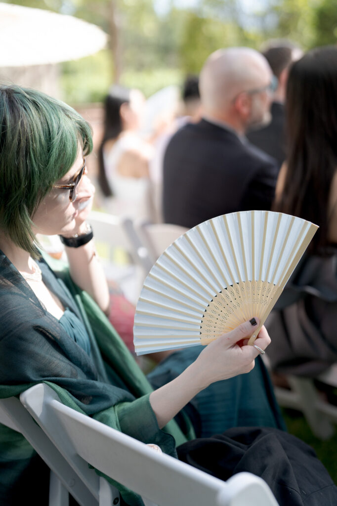 Female guest at a wedding officiation ceremony holds a folding fan.