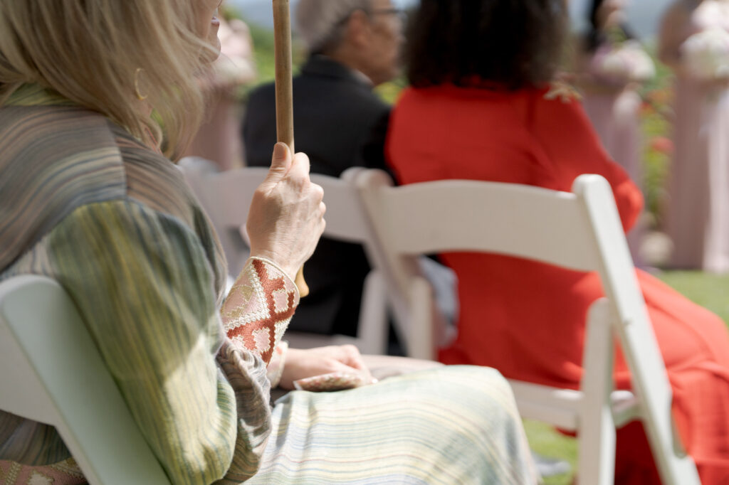 Seated guest at a wedding ceremony holds an umbrella.