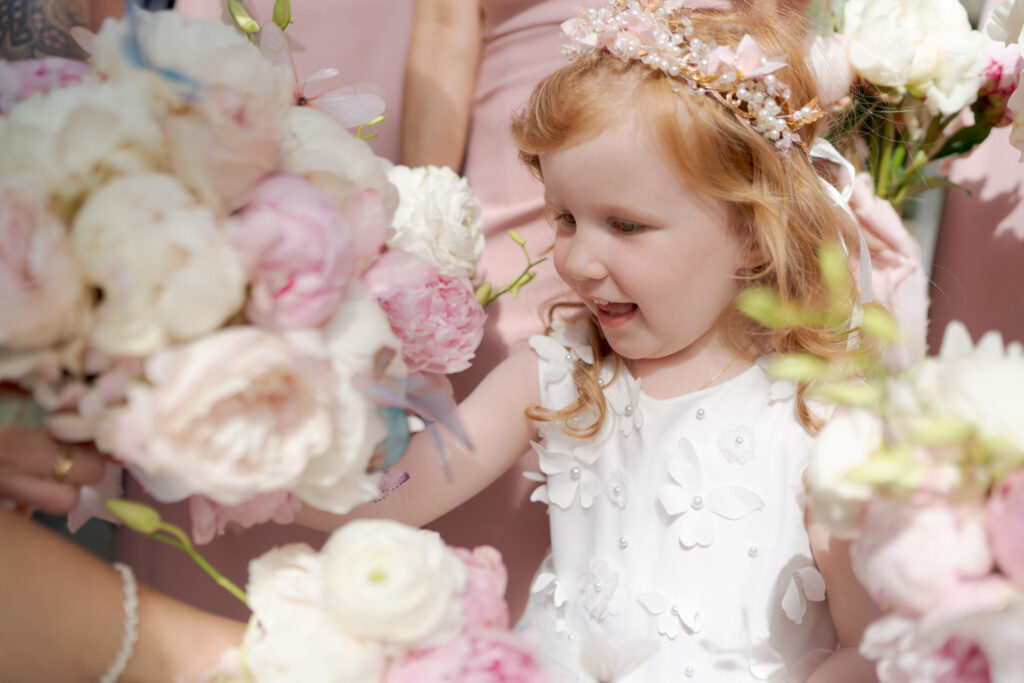 Cute little girl with white butterfly-stiched dress between bouquets of flowers.