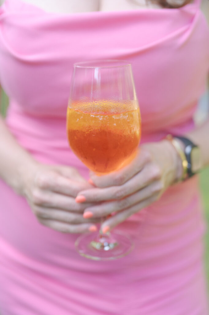 Elegant guest in pink dress and painted nails holds a glass of drink.