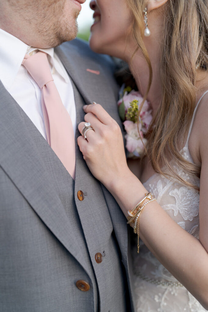 Close-up of a bride and groom embracing each other. The bride has ear pieces, bracelets, and a wedding ring on her finger.