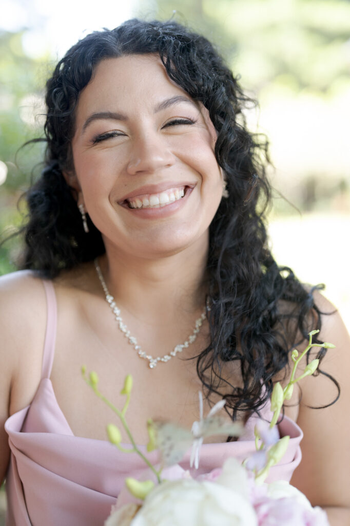 Beautiful bridesmaid wearing a diamond necklace and a pink dress smiles heartily.