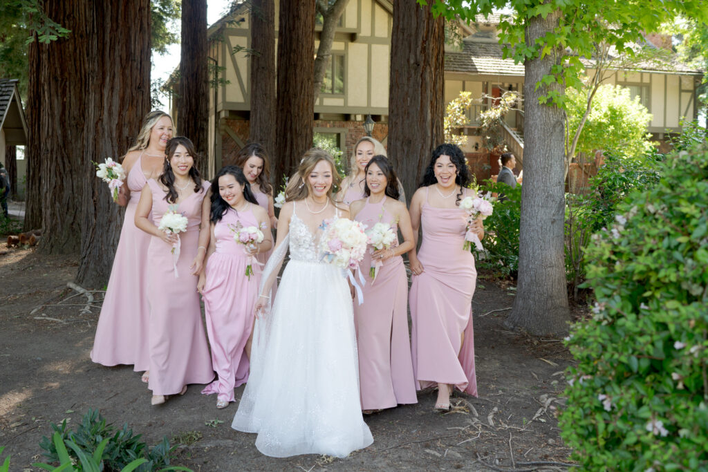 Elegantly dressed bride and her bridesmaids in front of large tree trunks.