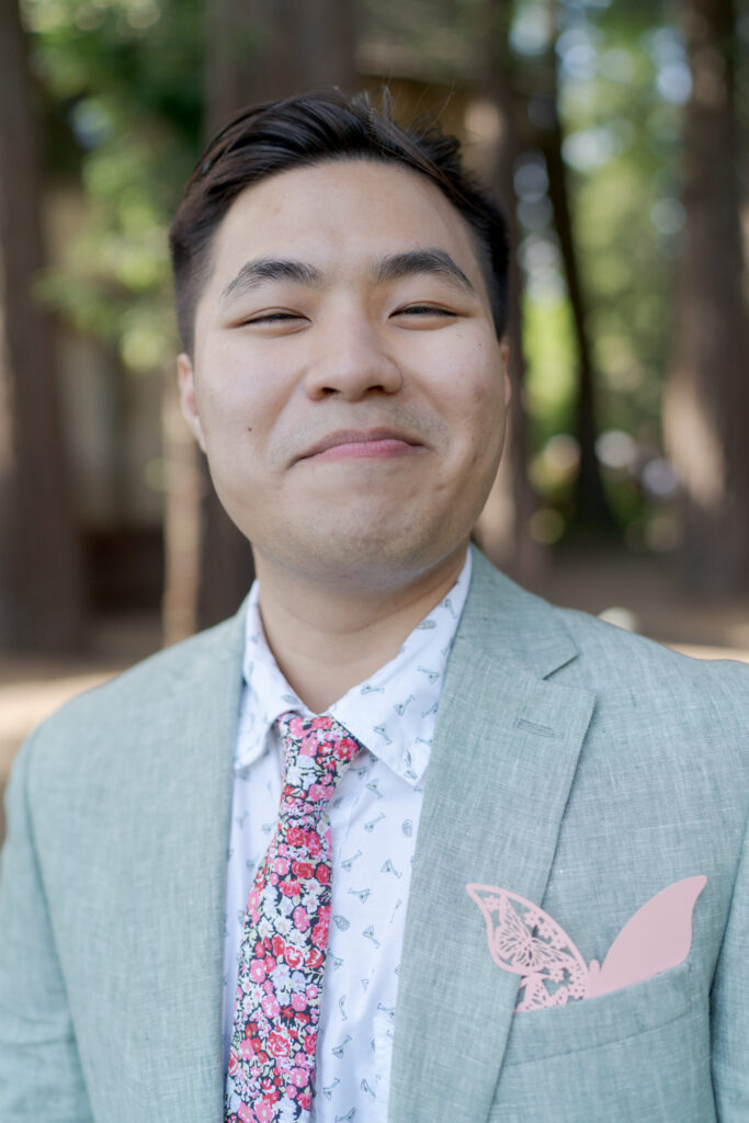 Happy male wedding guest dressed in suit and tie smiles at Robin Jolin's camera.