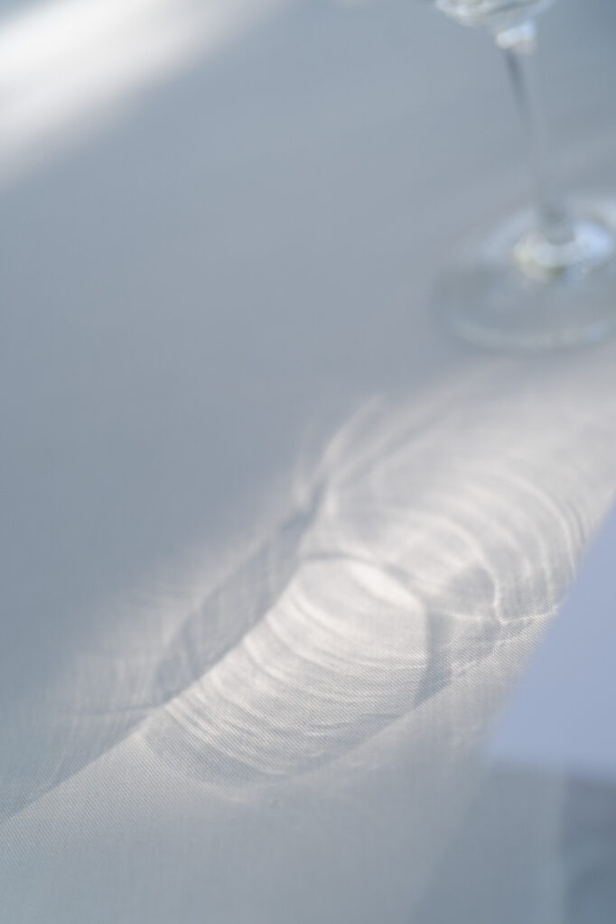 Aesthetic image of sunlight passing through a glass on a white tablecloth.