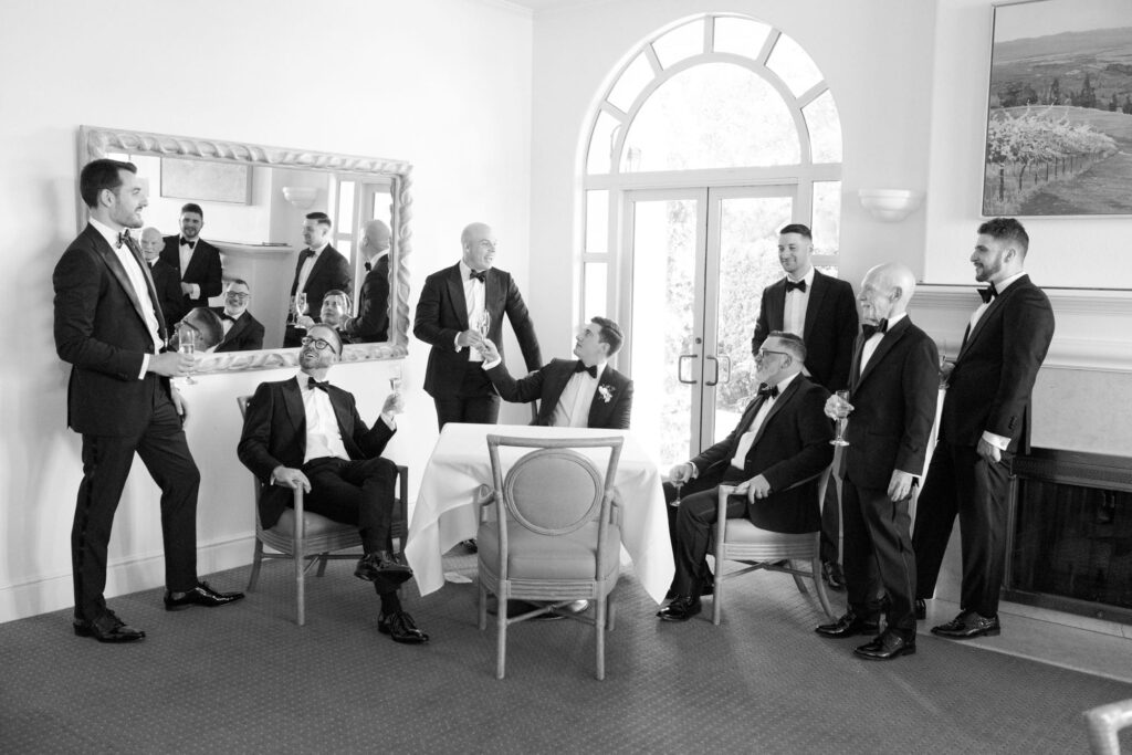 Young and old gentlemen dressed in classy black suits lounge around a table.