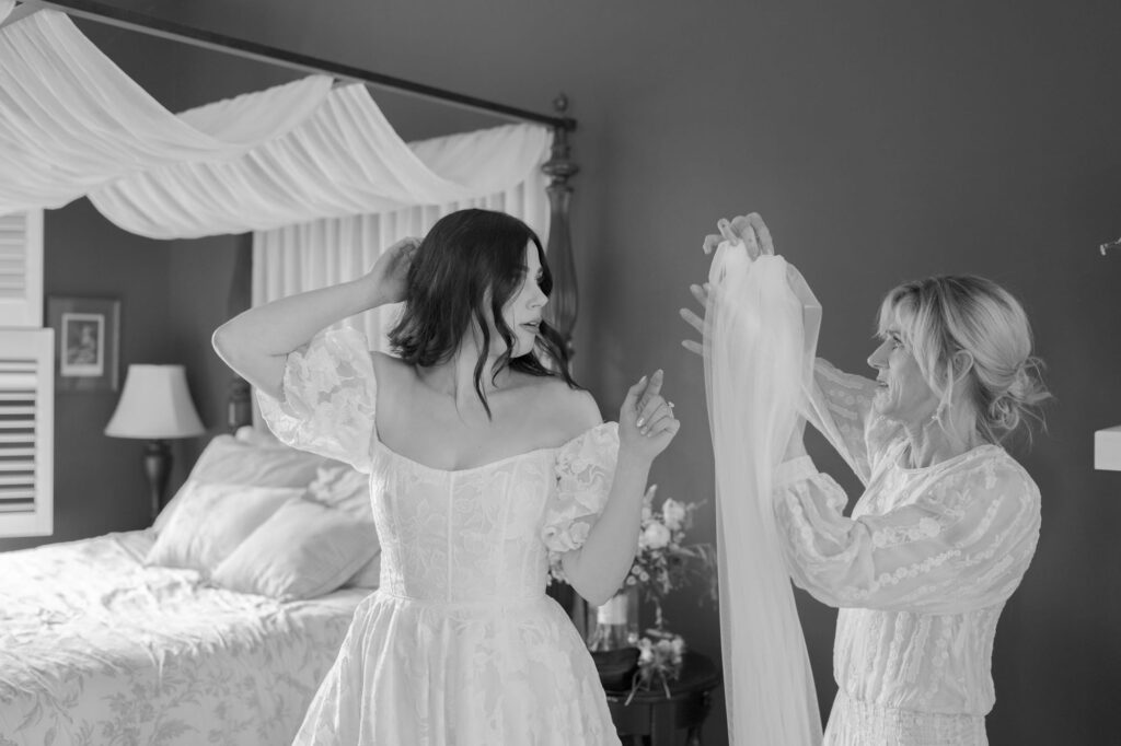 Bride getting ready for her wedding ceremony. A lady is helping her put on her wedding veil.