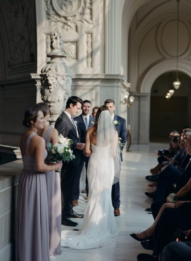 Wedding officiation ceremony in San Francisco City Hall with the bride, groom, officiator, best men, bridesmaids, and guests.