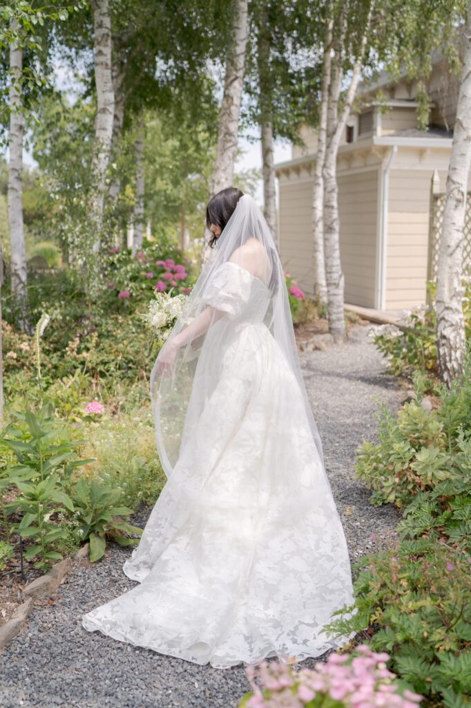 Bride in her wedding dress poses on a narrow garden trail.