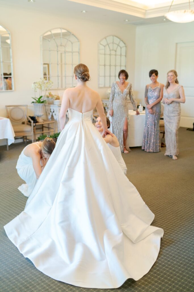 Bridesmaids help the bride with her wedding gown with a long train.