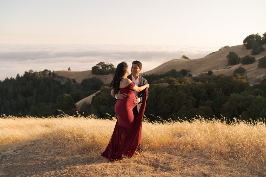 Man in suit embraces his pregnant wife atop Mt. Tam for maternity photo session.