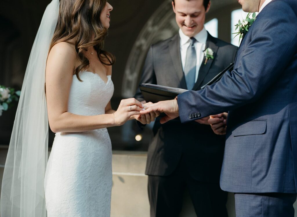 Bride puts on the ring to her groom in front of a wedding officiator.