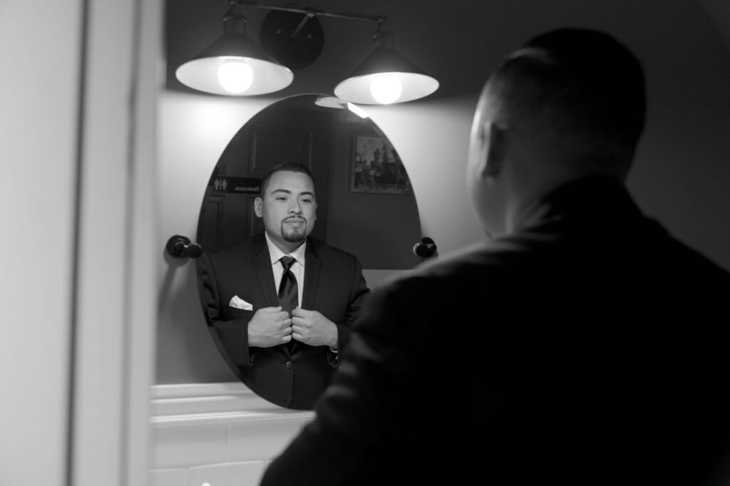 Handsome bridegroom checks himself in the mirror and adjusts his suit jacket.